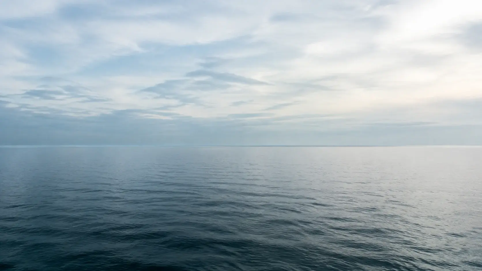 曇り空と穏やかな青緑の海。霞の中に続く水平線。